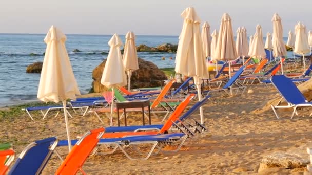 Роскошный отдых на Черном море, Болгария. Пустые разноцветные шезлонги или шезлонги и сложенные пляжные зонтики на курортном пляже — стоковое видео