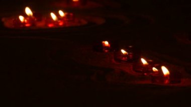 Kırmızı yuvarlak, Katolik tapınağında kumların üzerinde cenaze mumları yakıyor. Karanlıkta mum ışığı