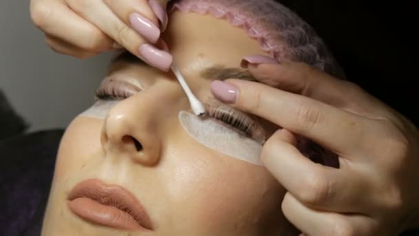 专业美容师从给年轻漂亮的女人涂上彩色睫毛的油漆中清除睫毛 — 图库视频影像