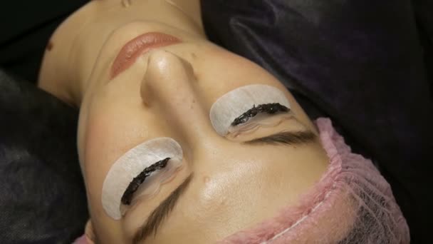 Young woman lies on the procedure for dyeing eyelashes with special black paint — Stock Video