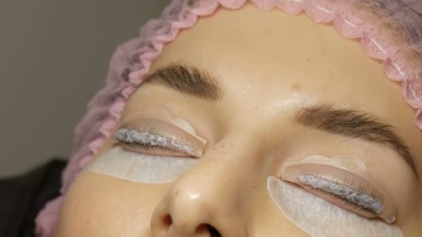 Professional eyelash enhancement in a beauty parlor. Special agent is applied to eyelashes on the face of a young woman — Stock Video