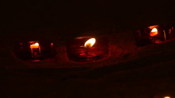 Rode ronde brandende begrafeniskaarsen op zand in een katholieke tempel. kaarslicht in het donker — Stockvideo