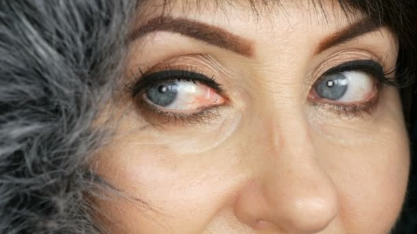 Mujer adulta de mediana edad con hermosos ojos azules grandes, maquillaje brillante, flechas pintadas y pestañas falsas en una capucha de piel sintética sobre fondo blanco — Vídeos de Stock