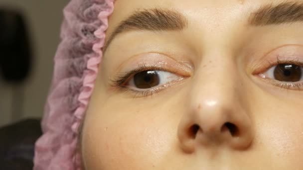 Cerrar la cara de la hermosa mujer joven con cejas peludas anchas y ojos marrones en un sombrero rosa antes del procedimiento para laminar las pestañas en un salón de belleza — Vídeos de Stock