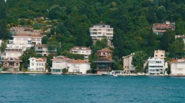 Deniz kıyısındaki yeşil tepelerdeki konut binalarının zengin lüks köşeleri yeşilliklerle çevrili. İstanbul, Türkiye 'den geçen bir tekneden görüntü
