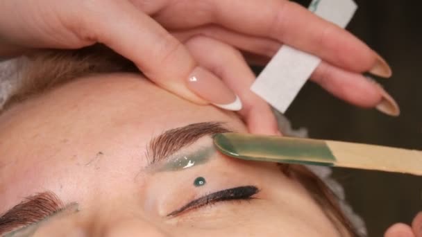 Correção de cera da forma das sobrancelhas. Esteticista aplica cera verde quente em sobrancelhas e remove o excesso de cabelo com tira especial . — Vídeo de Stock