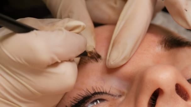 Microblading eyebrow tattoo, permanent makeup. Master in gloves, using special needle, injects pigment into the skin and stains the eyebrows using hair technique, making them natural, close-up view — Stock Video