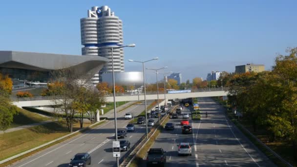 München, Duitsland - 25 oktober 2019: Hoofdkantoor van Bmw in München. De toren wordt vaak genoemd als een van de meest opvallende voorbeelden van architectuur in München. Auto 's die over de weg passeren — Stockvideo