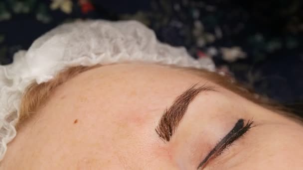 Eine Kosmetikerin in Handschuhen trägt mit einer speziellen Nadel ein Farbpigment unter die Haut der Augenbrauen auf. Augenbrauen-Formkorrektur mit Haarmikroblutungen, Permanent Make-up, Augenbrauen-Tätowierung — Stockvideo