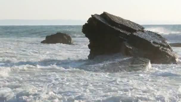 Zonsopkomst of zonsondergang op zee. Mooie grote stormachtige golven met schuim bedekken enorme rotsen en rotsblokken aan wal — Stockvideo