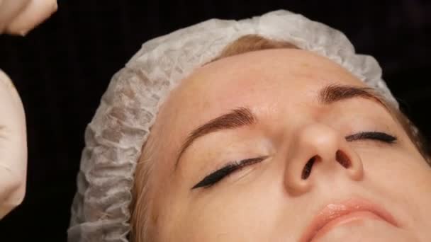 Mikroblading Haarbraue. Augenbrauen-Tätowierung und dauerhaftes Make-up. Eine Kosmetikerin mit Handschuhen entfernt das Farbpigment auf der Haut der Augenbrauen. — Stockvideo