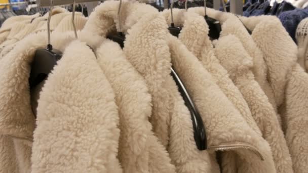 Ciepłe białe kurtki zimowe wiszą na wieszaku w butiku damskiej odzieży — Wideo stockowe