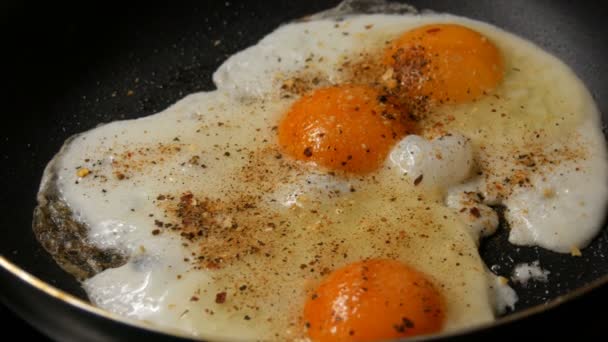 Close-up view of fried eggs in pan sprinkled with spices and dry onions — Stock Video