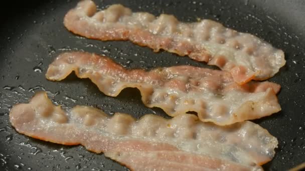 Fatias finas de bacon são fritas em óleo de girassol em panela quente com revestimento antiaderente vista de perto — Vídeo de Stock