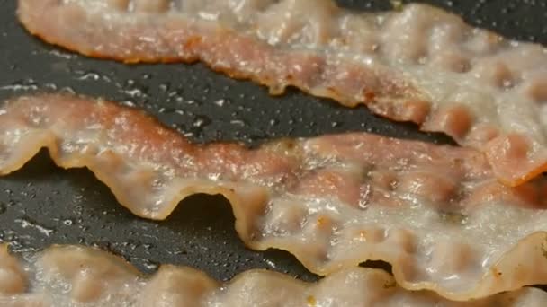 Dunne plakjes spek worden gebakken in zonnebloemolie in hete pan met anti-aanbaklaag van dichtbij bekeken — Stockvideo