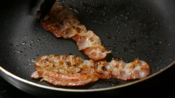 Fette sottili di pancetta vengono fritte in olio di girasole in padella calda con rivestimento antiaderente. Man Chef cucina per la prima colazione, trasformando un incredibile pancetta croccante — Video Stock