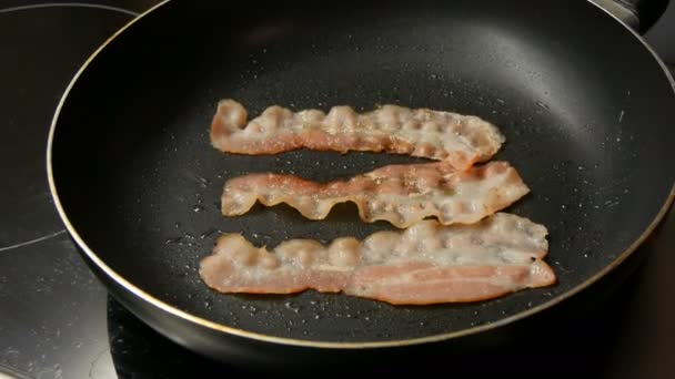 Thin slices of bacon are fried in sunflower oil in hot pan with non-stick coating. Man Chef cooking for breakfast, turning an amazing crispy bacon — 비디오