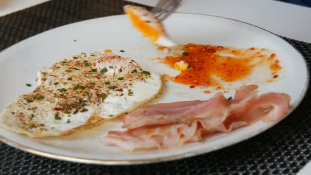 Mężczyzna arystokrata jedzenie rano jajecznica smażone jajka z boczkiem i czerwony sos na białym talerzu z nożem i widelcem — Wideo stockowe