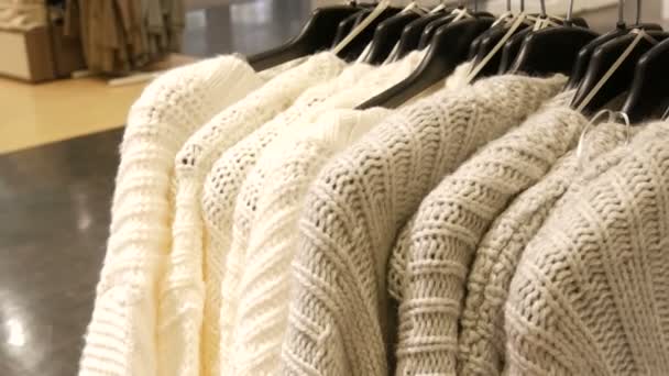 美しい女性は、衣料品店でハンガーに光色のセーターを編んだ — ストック動画