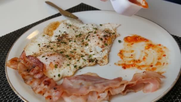 Man aristokrat äta morgon äggröra stekta ägg med bacon och röd sås på vit tallrik med en kniv och gaffel — Stockvideo