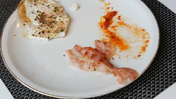 Aristócrata macho comiendo huevos fritos revueltos por la mañana con tocino y salsa roja en un plato blanco con un cuchillo y tenedor — Vídeos de Stock