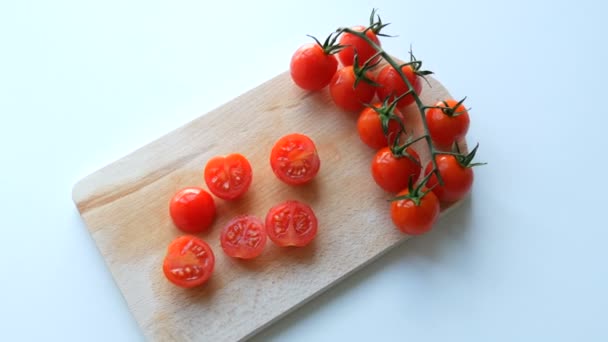Tomates cereja pequenos vermelhos maduros em um monte de clusters e parcialmente cortados na placa da cozinha e fundo branco — Vídeo de Stock