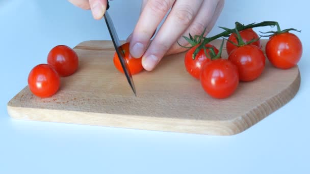 Weibliche Hände schneiden schöne saftige reife rote Kirschtomaten in Zweigen auf weißem Tischhintergrund und hölzernem Küchenbrett — Stockvideo