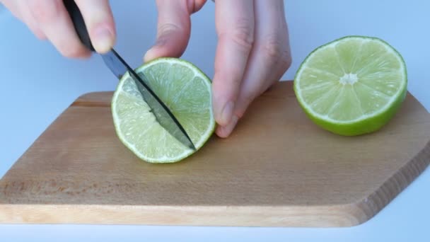 Female hands cut ripe green lime on white table and home wooden kitchen board — 비디오