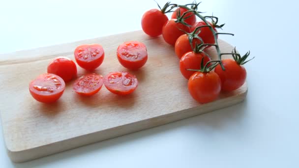 Стиглі червоні маленькі вишневі помідори в купі скупчень і частково нарізані на кухонній дошці і білому тлі — стокове відео