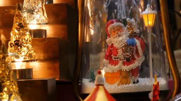 人工雪が市場のカウンターに落ちる美しい居心地の良い明るいクリスマスライトとサンタクロースの置物 — ストック動画