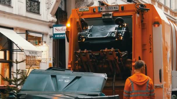 Wenen, Oostenrijk - 21 december 2019: Vuilniswagen tilt plastic vuilnisbakken op en gooit afval in de machine. Straatreiniging, mannen die afval uit vuilnisbakken laden. — Stockvideo