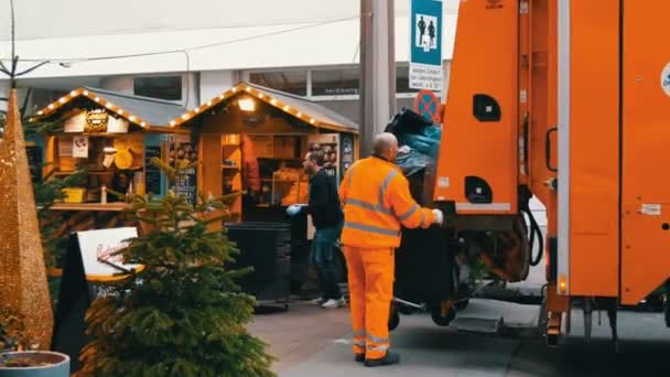 Βιέννη, Αυστρία - 21 Δεκεμβρίου 2019: Σκουπιδιάρικο που σηκώνει πλαστικά σκουπίδια και πετάει σκουπίδια μέσα στο μηχάνημα. Καθαρισμός δρόμων, άντρες που φορτώνουν απόβλητα από κάδους. — Αρχείο Βίντεο