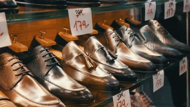 Estantes en la ventana de la tienda de zapatos con diferentes zapatos clásicos de cuero para hombre en varios colores con etiquetas de precios con ventas de descuento — Vídeos de Stock
