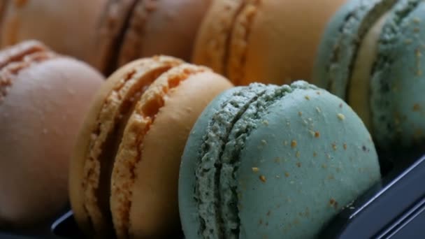 Többszínű francia süti macaron egy speciális fekete dobozban egy fehér asztalon. Színes torta macaroon egy ajándékdobozban közelről — Stock videók