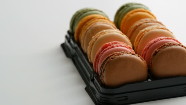 Többszínű francia sütik macaron vagy macaroon egy speciális fekete doboz fehér asztalon — Stock videók