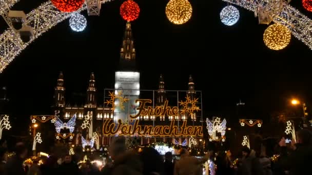 Вена, Австрия - 21 декабря 2019 года: Рождественский рынок перед ратушей. Празднично украшенная площадь с гирляндами, рядом с которой ходят туристы и местные жители. Столовые с различными продуктами питания и вещи — стоковое видео