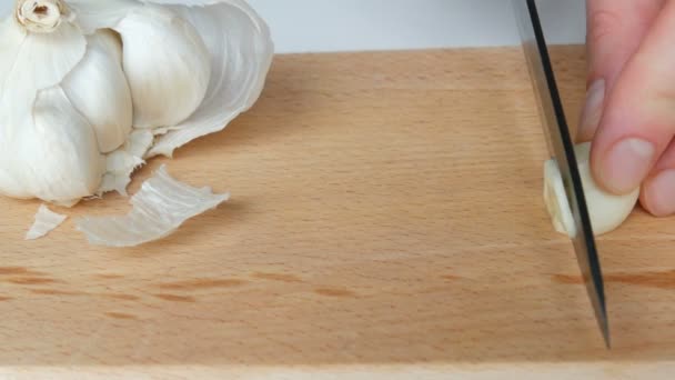 Dłonie kobiet wyciąć biały czosnek na drewnianej płycie kuchennej z czarnym nożem ceramicznym — Wideo stockowe
