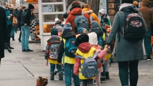 Nürnberg, Németország - 2019. december 10.: Fényvisszaverő mellényes óvodáskorú kisgyermekek egy csoportja sétál az utcán a dadákkal sorba állított kirándulásokon. — Stock videók