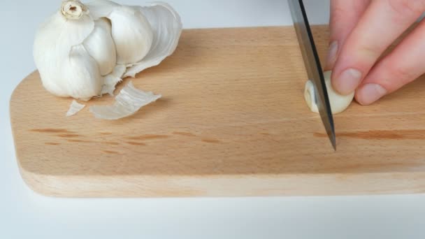 Female hands cut white garlic on a wooden kitchen board with black ceramic knife — 비디오