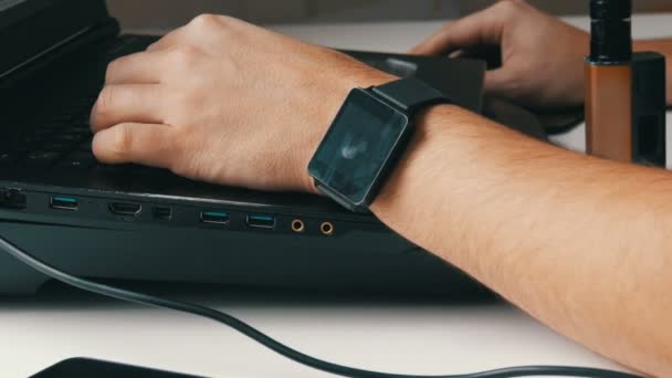 Ein Mann arbeitet am Laptop. Männerhände mit Smartwatch und elektronischer Zigarette tippen auf der Tastatur. — Stockvideo