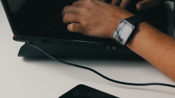 Un homme travaille sur un ordinateur portable. Les mains des hommes avec une montre intelligente et une cigarette électronique tapent sur le clavier . — Video