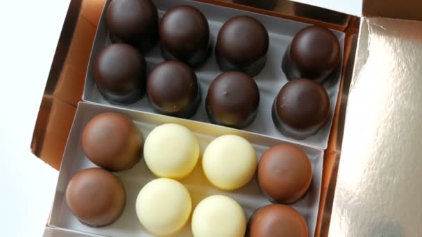Bizarr, szellős szuflé desszertek, édességek formájában, fehér, fekete és tejcsokoládé mázában. Egy doboz csokoládé a fehér asztalon — Stock videók