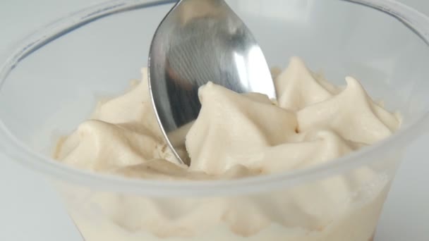 Dessert of whipped cream and chocolate in plastic cup. Female hand with teaspoon removes the top of the cream — 비디오