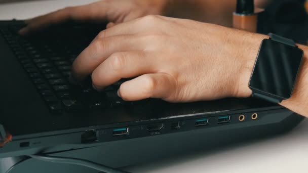 Un hombre trabaja en el portátil. Mens manos con un reloj inteligente y un cigarrillo electrónico están escribiendo en el teclado . — Vídeos de Stock