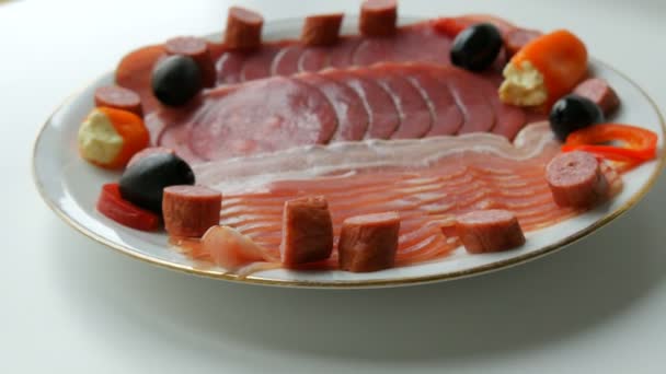 Carne y lonchas de salchicha en plato junto a aceitunas negras, pimentón con queso y salchichas de caza. Placa de carne curada — Vídeos de Stock