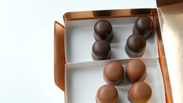 En halvtom låda med luftiga desserter av sufflé Bizze i form av sötsaker i glasyr av vit, svart och mjölkchoklad. Chokladask på ett vitt bord — Stockvideo