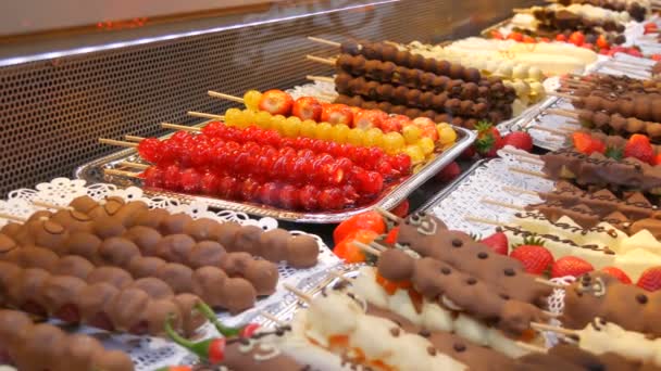 Diverse vruchten op een houten spiesen stok in gekarameliseerde glazuur gemaakt van melk zwarte witte chocolade. Druiven, banaan, aardbeien in glazuur op de toonbank van de kerstmarkt — Stockvideo