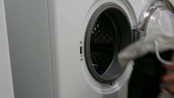 Erkekler çamaşır ve çamaşırları çamaşır makinesine doldurur. Çamaşır odasında büyük beyaz çamaşır makinesi var.. — Stok video