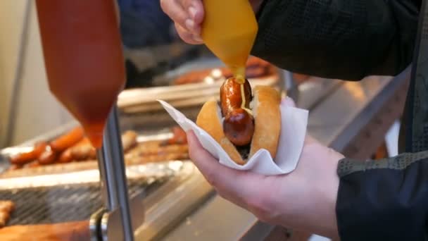 Hot Dog. Utcai gyorskaja. A hím kéz egy kolbászt tart zsemlében, és mustárral, speciális tartályokba önti.