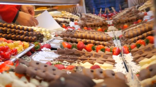 Varias frutas en un palo de madera pincho en esmalte caramelizado hecho de leche chocolate blanco negro. Uvas, plátano, fresas en la guinda en el mostrador del mercado de Navidad — Vídeos de Stock